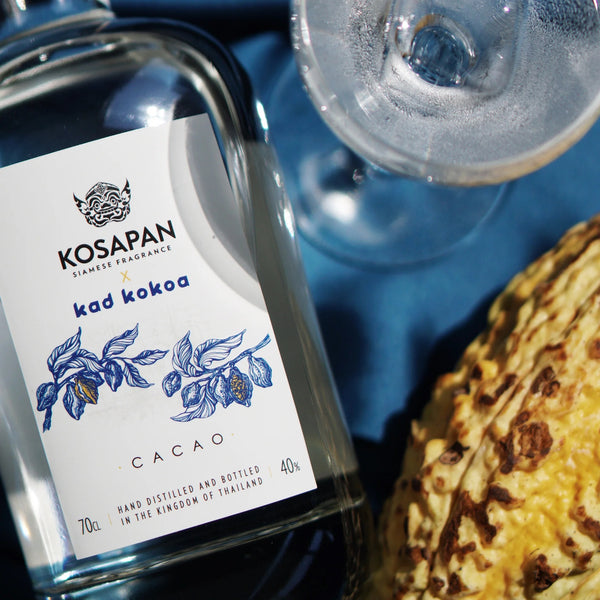 Kosapan Kad Kokoa Cacao Spirit bottle with a glass and Cocoa seed on a blue cloth in background